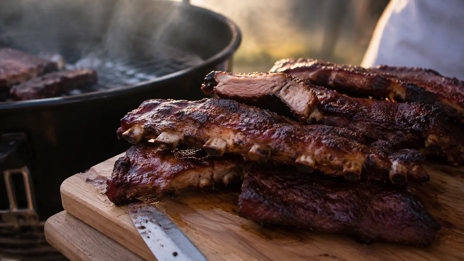 A rack of ribs resting on a cutting board with light smoke in the background